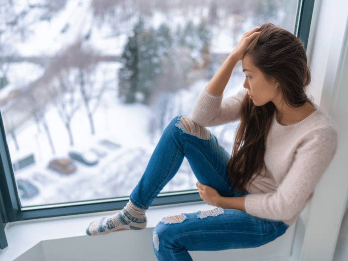 female student with a hand to her forhead looks out a window to the wintery scene below